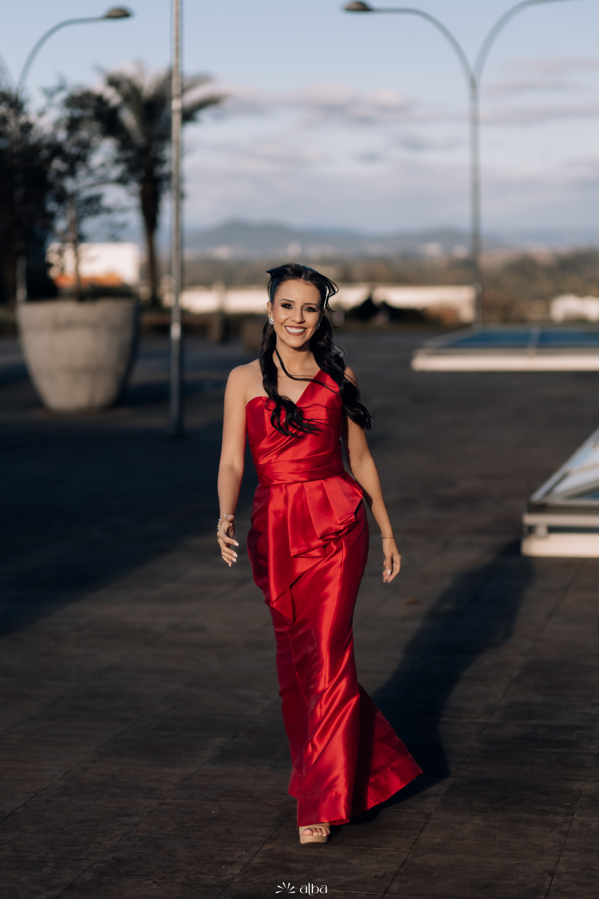 Retrato vertical de Lígia caminhando em direção à câmera com vestido vermelho no campus da Univates.