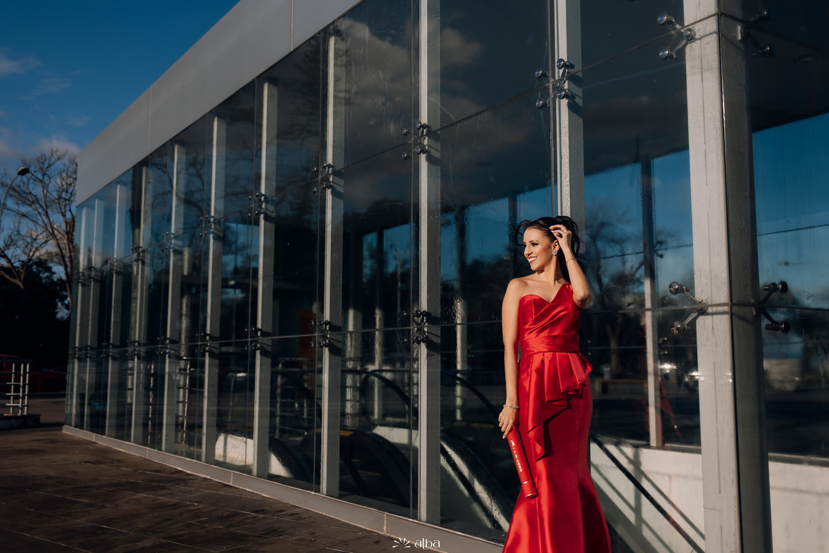 Lígia posando junto à fachada envidraçada moderna da Univates, segurando o canudo.