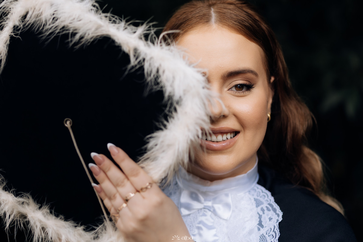 Retrato criativo de formanda segurando o capelo com plumas, mostrando parte do rosto – Alba Estúdio, Lajeado.