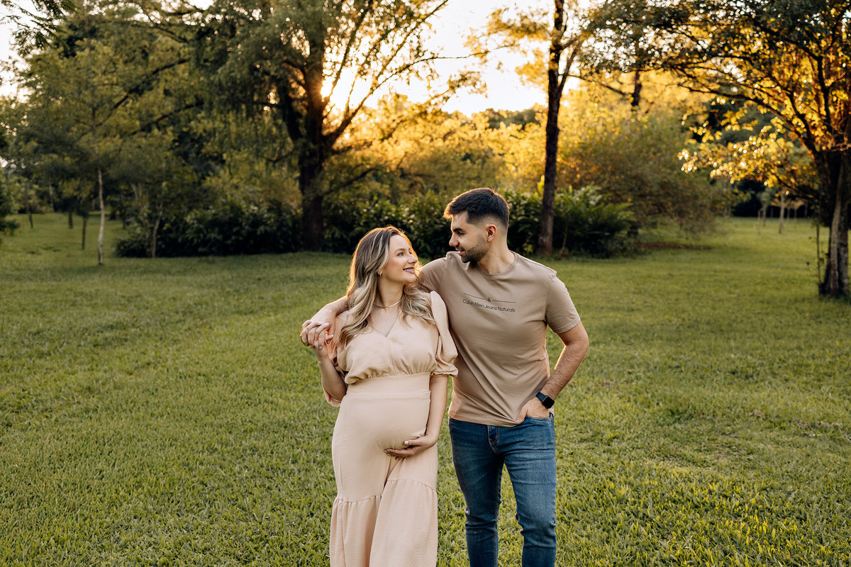 Casal caminhando abraçado durante ensaio gestante ao ar livre, com luz suave e natural de fim de tarde – fotografia por Alba Estúdio.