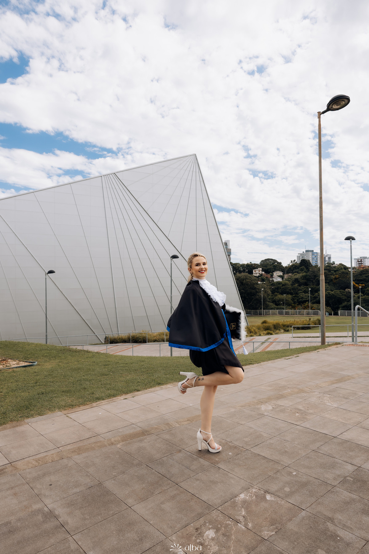 Foto de formatura da Samara na Univates, em Lajeado, usando beca em frente à arquitetura do campus, pelo Alba Estúdio.