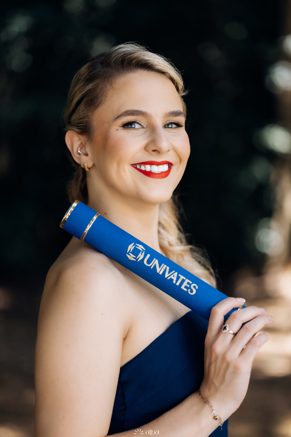 Retrato de formatura da Samara na Univates, em Lajeado, com canudo azul e olhar sorridente, fotografado pelo Alba Estúdio.