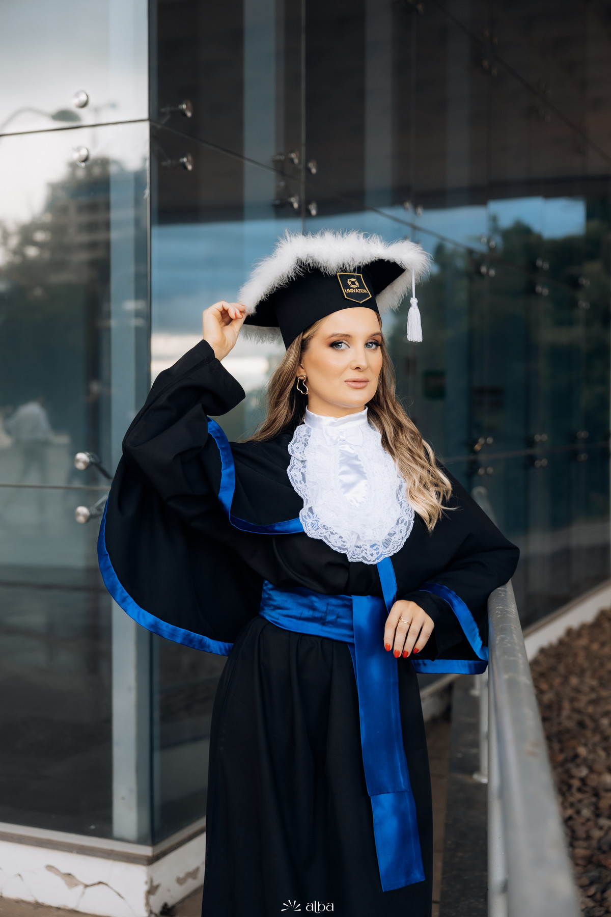 Retrato de formatura da Rafaela na Univates, em Lajeado, usando beca, capelo e faixa azul, fotografado pelo Alba Estúdio.