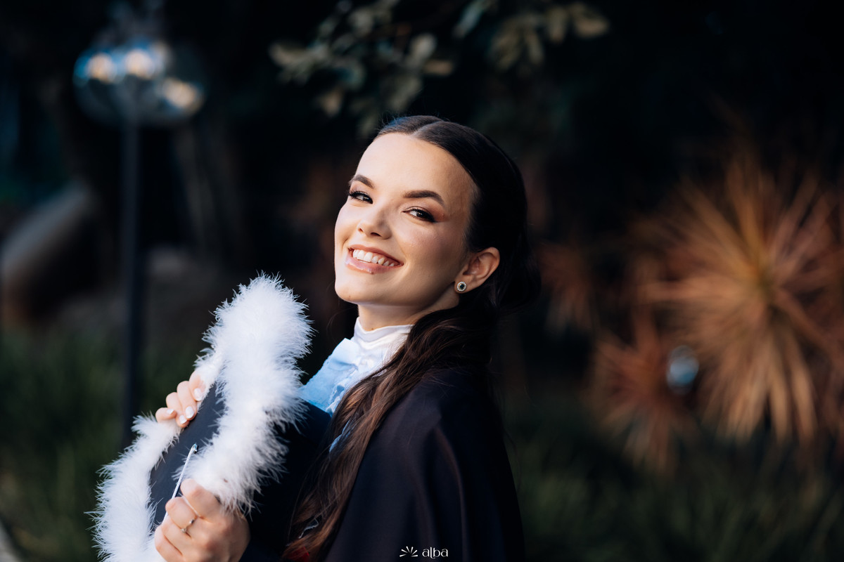 Retrato da formanda Alice na Univates, em Lajeado, sorrindo entre folhagens, fotografado pelo Alba Estúdio.