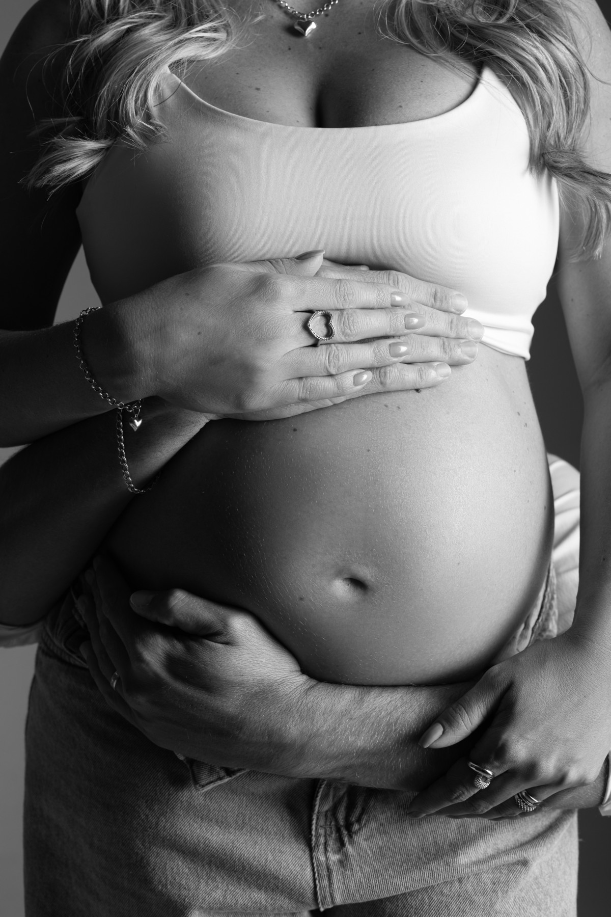 Detalhe em preto e branco da barriga de gestante envolvida pelas mãos do casal, destacando afeto, espera e conexão. Ensaio realizado pelo Alba Estúdio em Lajeado, RS.