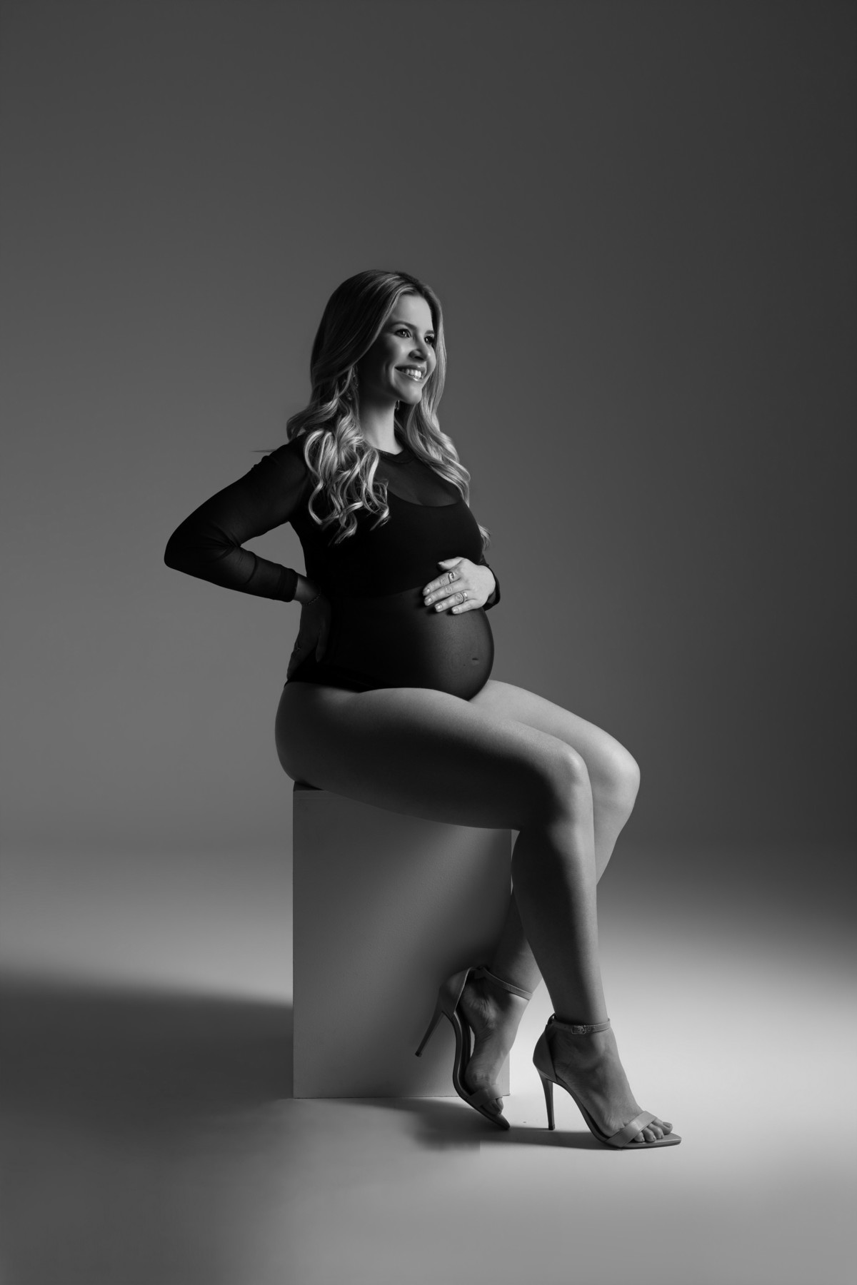 Retrato de gestante em preto e branco, sentada e sorrindo, com luz elegante e composição atemporal. Fotografia de maternidade do Alba Estúdio em Lajeado, RS.