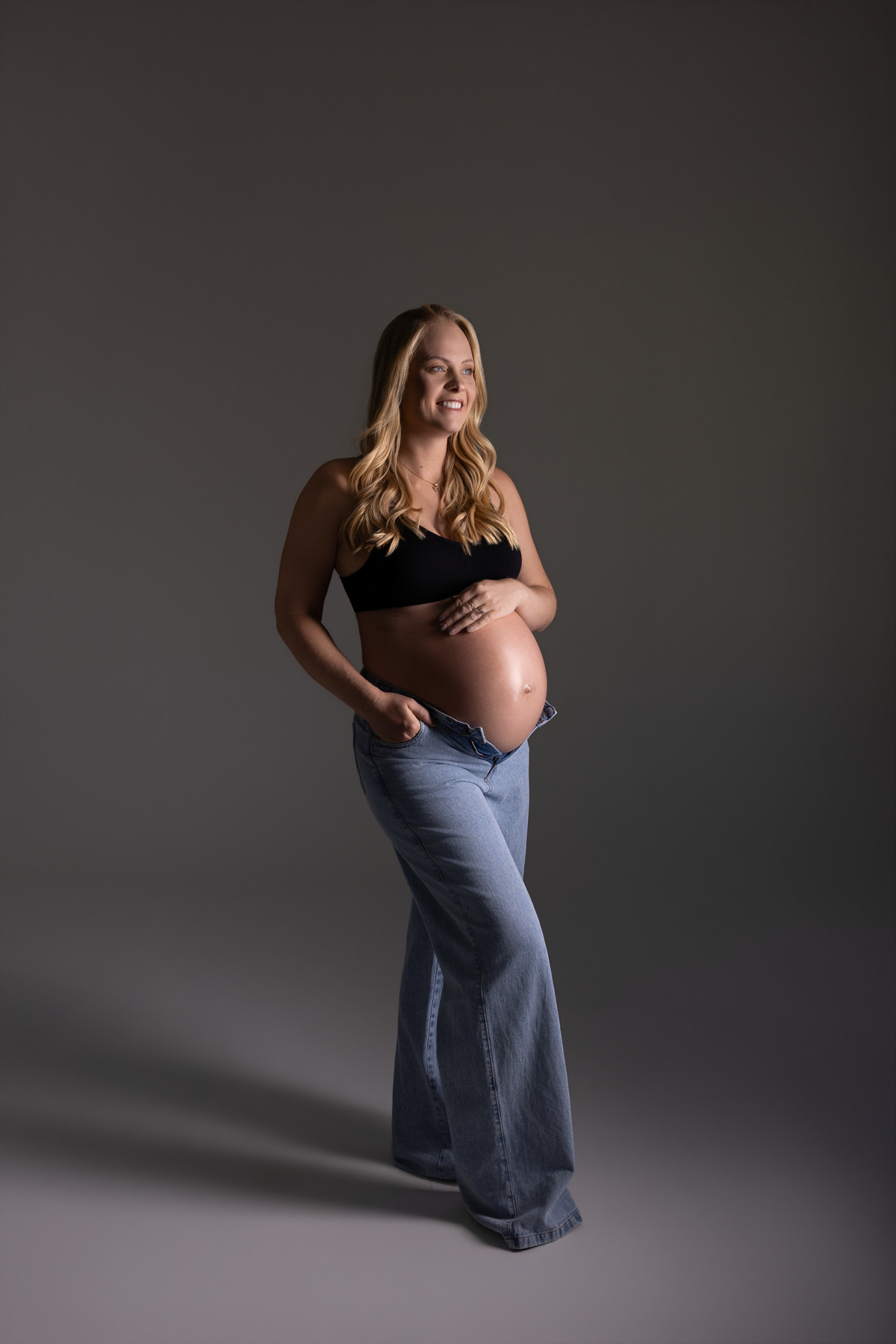 Retrato de gestante em estúdio com jeans e top preto, em uma proposta moderna, leve e elegante. Fotografia de gravidez do Alba Estúdio em Lajeado, RS.