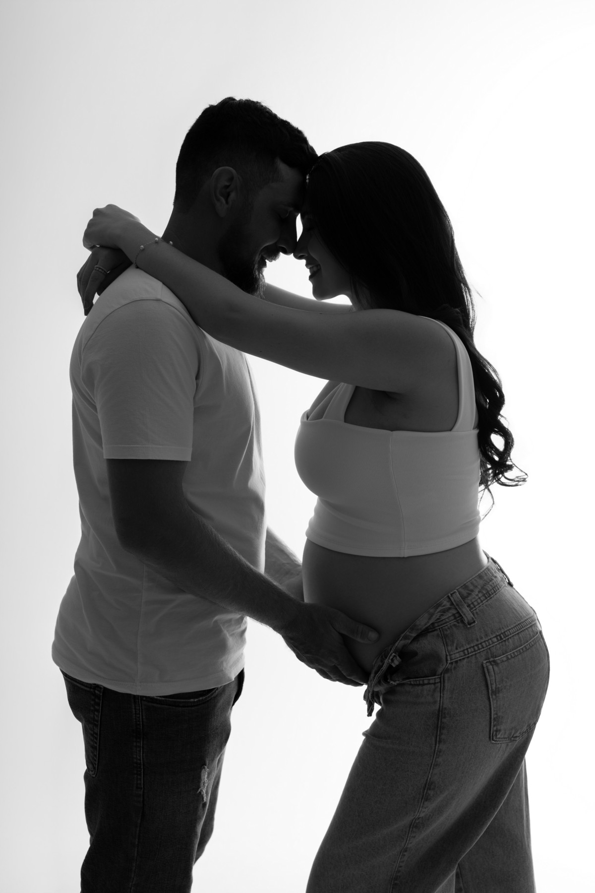 Ensaio gestante de casal em preto e branco, com luz de fundo, silhuetas e mãos sobre a barriga, destacando amor e conexão na espera por Lucca. Fotografia do Alba Estúdio em Lajeado, RS.