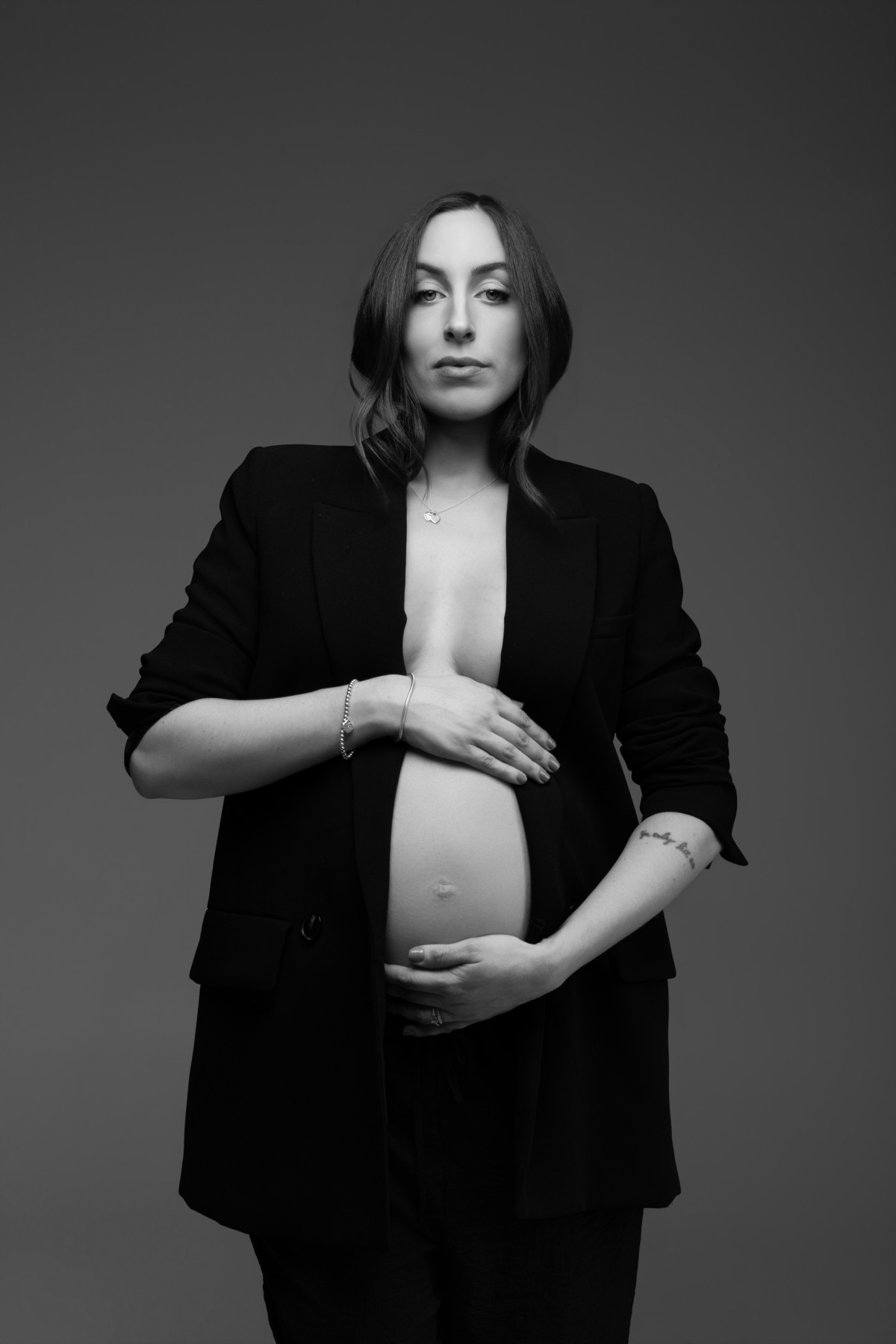 Retrato feminino em preto e branco durante ensaio gestante, com blazer preto e composição editorial que valoriza força e elegância. Fotografia do Alba Estúdio em Lajeado, RS.
