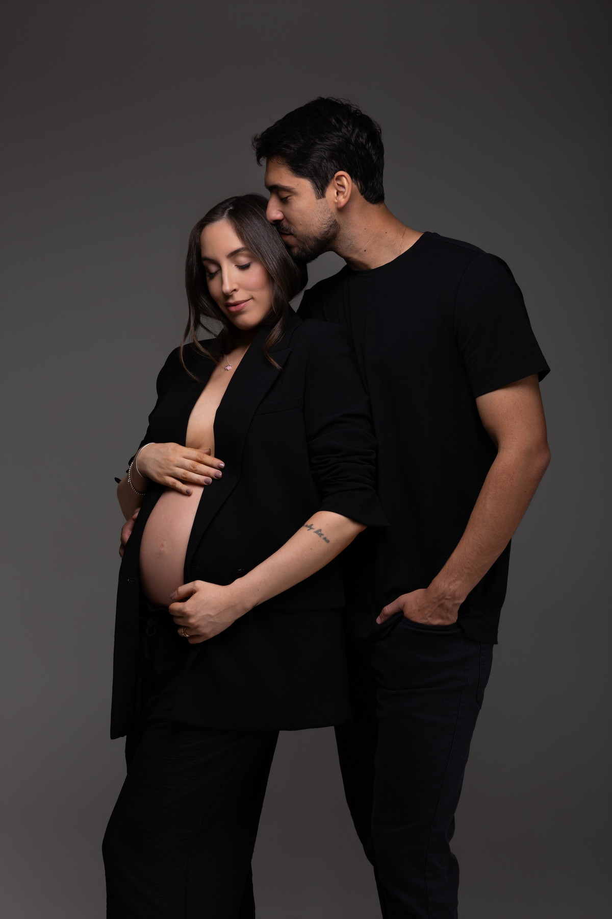 Retrato afetivo de casal em ensaio gestante, com beijo na cabeça e mãos envolvendo a barriga na espera por Pietro. Fotografia elegante do Alba Estúdio em Lajeado, RS.