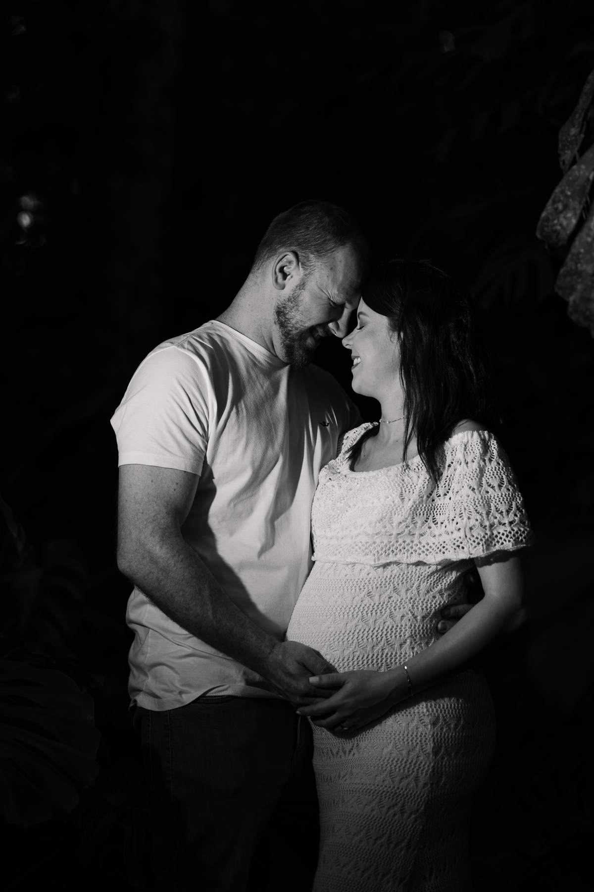 Retrato em preto e branco de casal abraçado com as mãos sobre a barriga da gestante | Fotografia de gravidez Alba Estúdio.