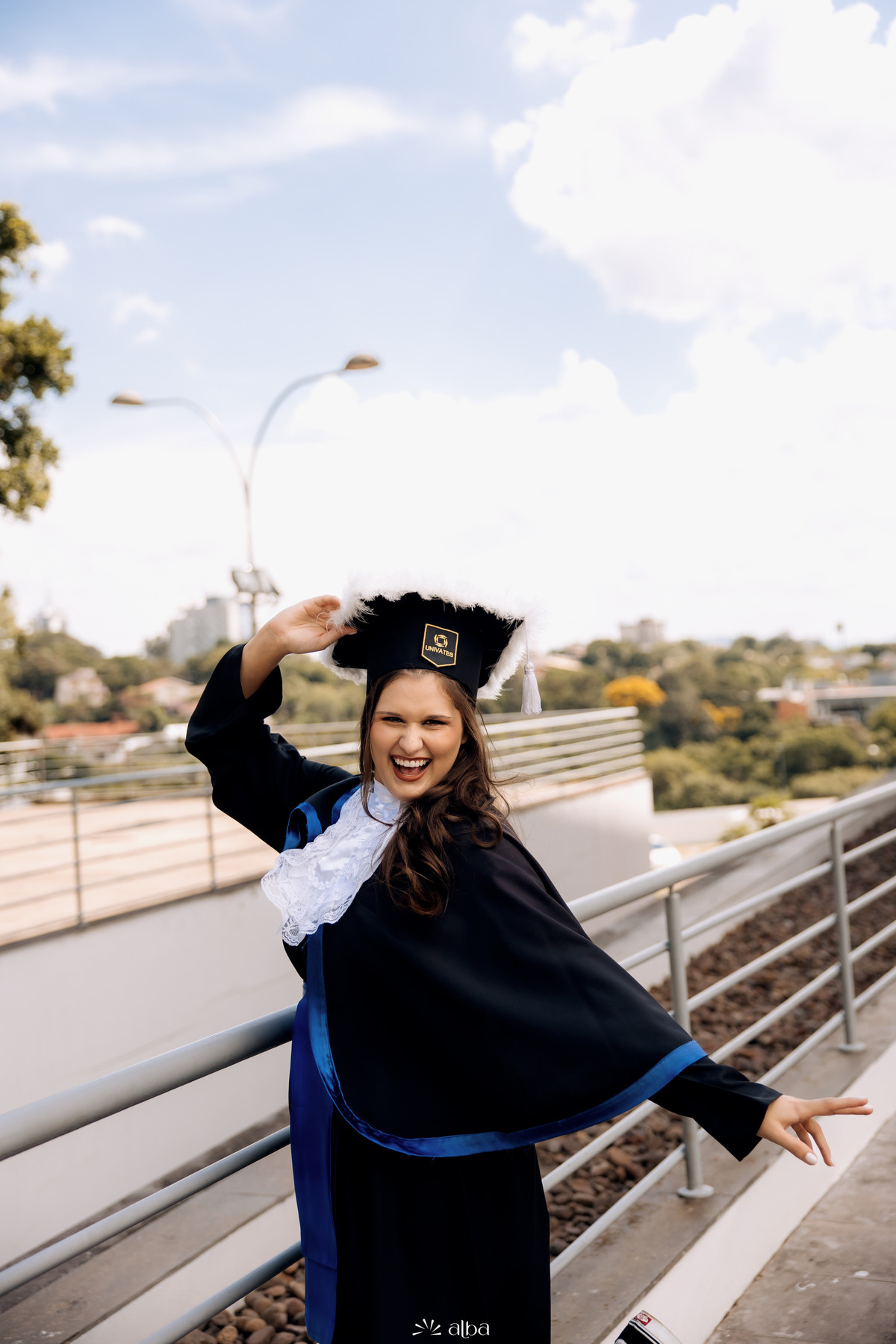 Formanda sorrindo com toga e capelo durante ensaio de formatura descontraído na Univates | Alba Estúdio, Lajeado RS.