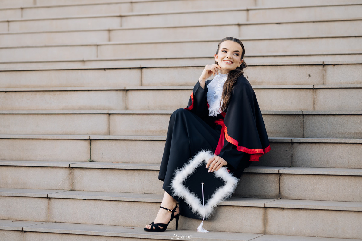 Formanda de toga sentada nas escadarias durante ensaio de formatura elegante na Univates | Fotografia Alba Estúdio.