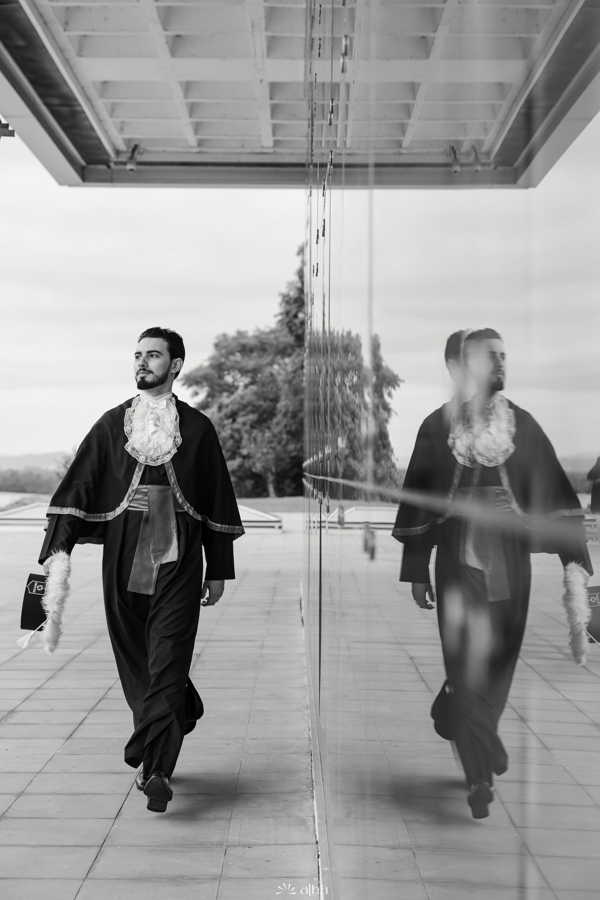 Formando caminhando de toga ao lado de parede espelhada durante ensaio de formatura moderno na Univates | Alba Estúdio.