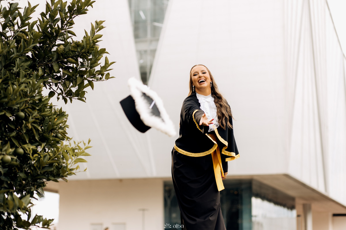 Formanda sorrindo ao lançar o capelo durante ensaio de formatura espontâneo na Univates, em Lajeado RS.