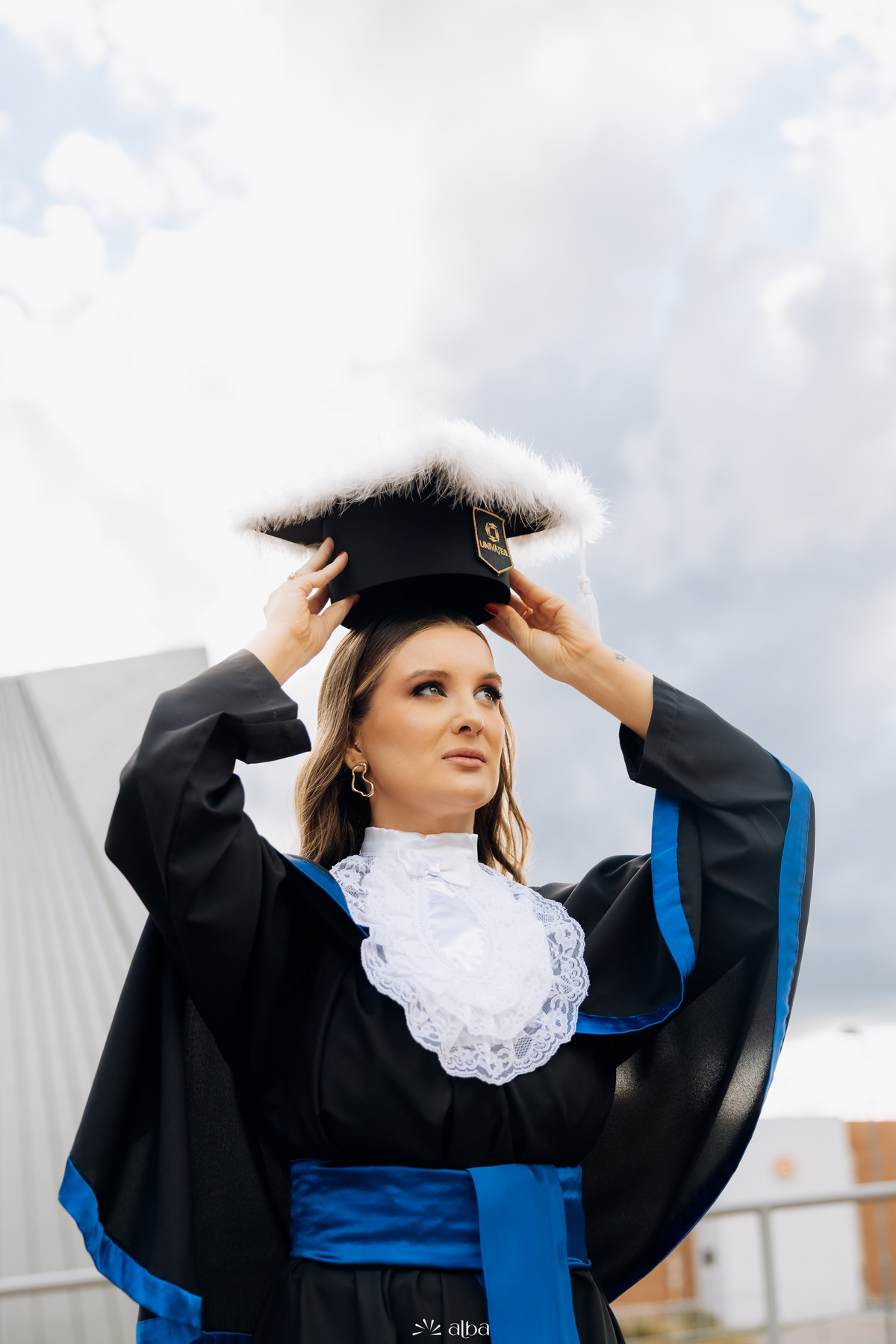 Formanda ajustando o capelo em retrato marcante com toga azul durante ensaio de formatura na Univates | Alba Estúdio, Lajeado RS.