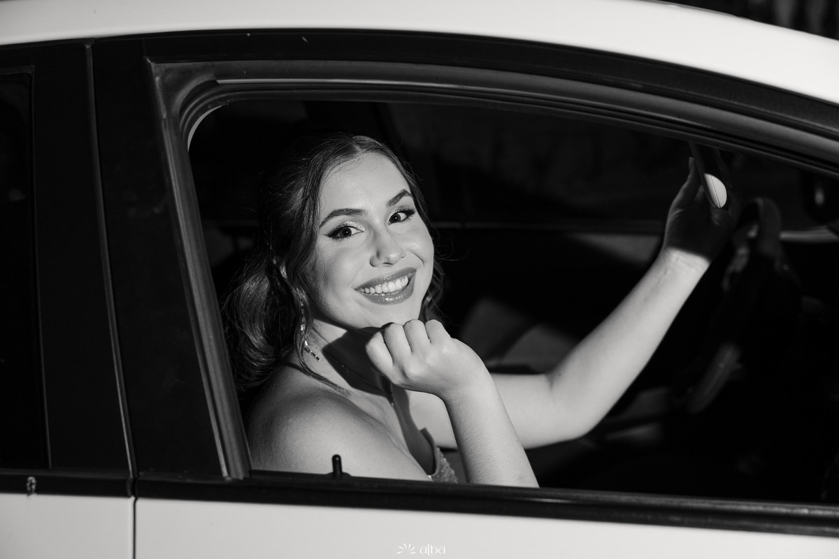Retrato em preto e branco de Ana Pellini sorrindo dentro do carro a caminho da festa de formatura | Alba Estúdio.
