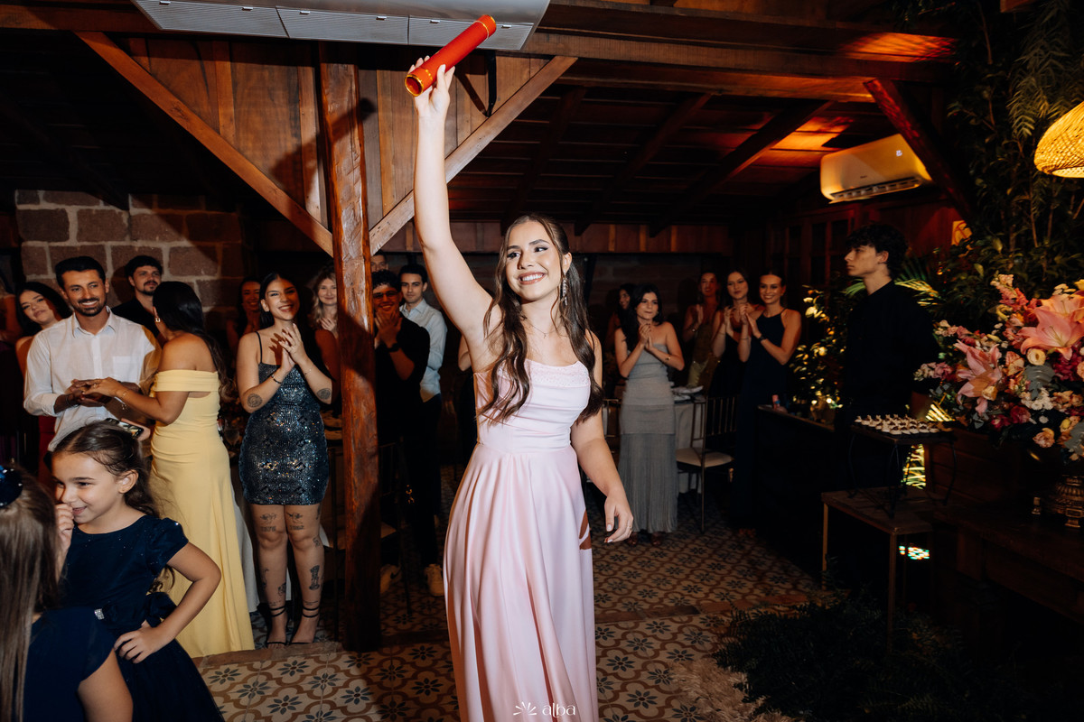 Entrada de Ana Pellini na festa de formatura, erguendo o diploma da Univates diante dos convidados na Casa Irmando.