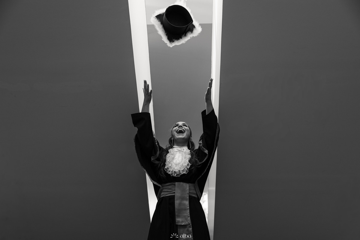 Formanda lançando o capelo em fotografia criativa em preto e branco no campus da Univates, em Lajeado RS.