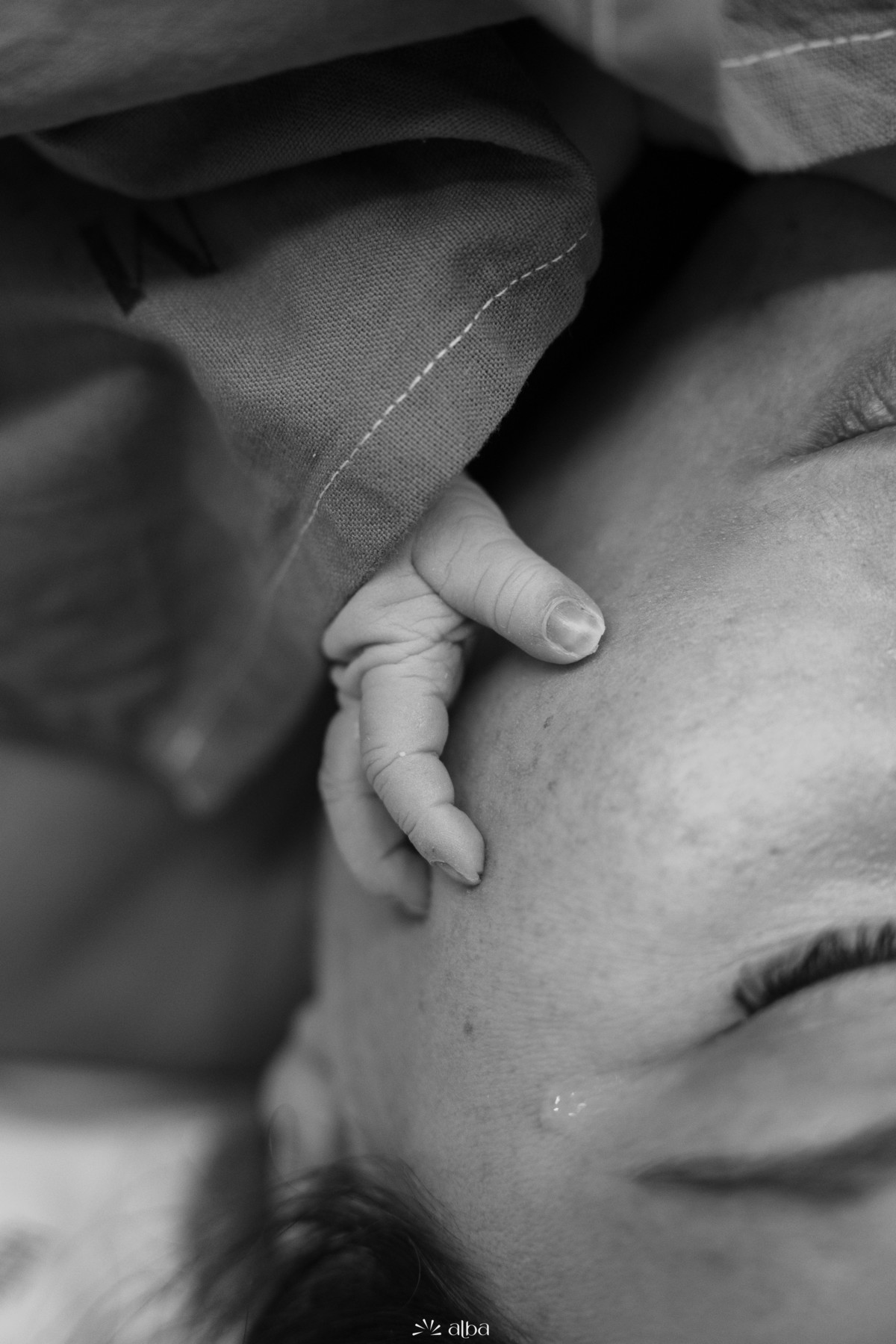 Pequena mão do recém-nascido sobre o rosto da mãe em um momento de emoção após o parto. Fotografia no Hospital Bruno Born, em Lajeado.