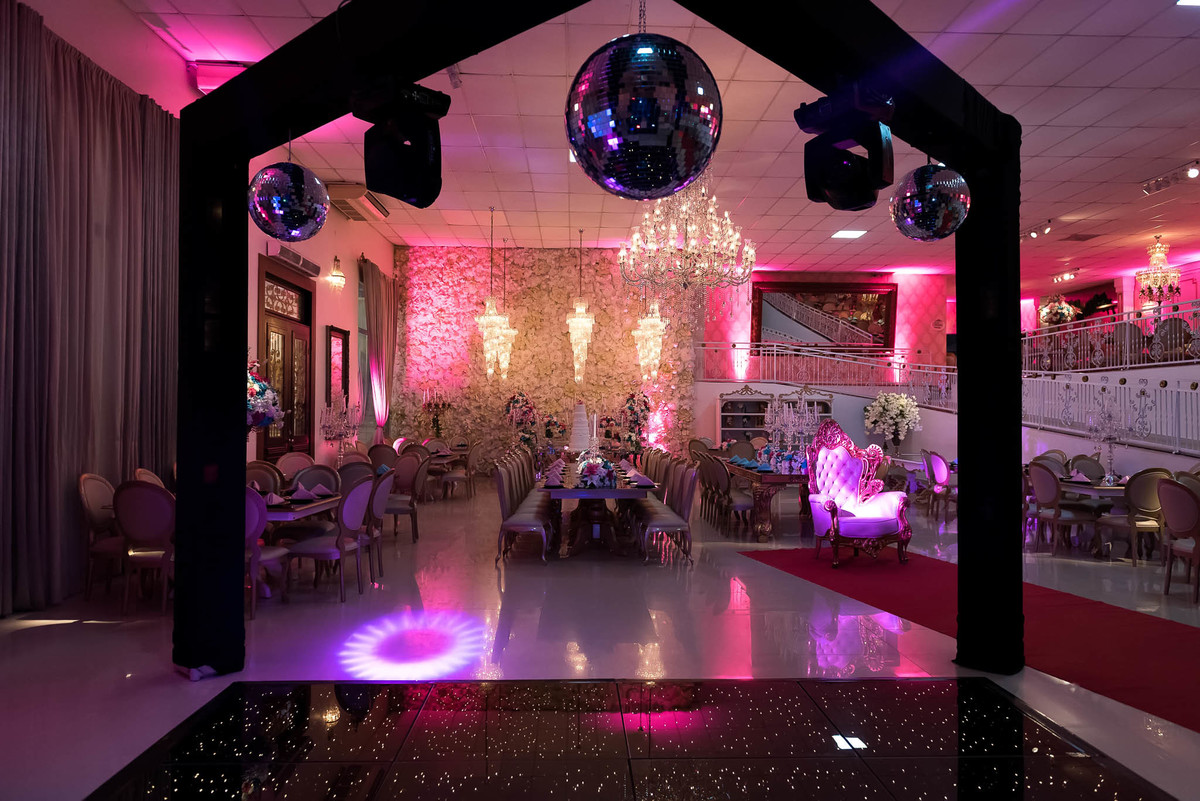 Visão panorâmica do salão de festas, com iluminação em tons de rosa e roxo, criando um ambiente vibrante e festivo
