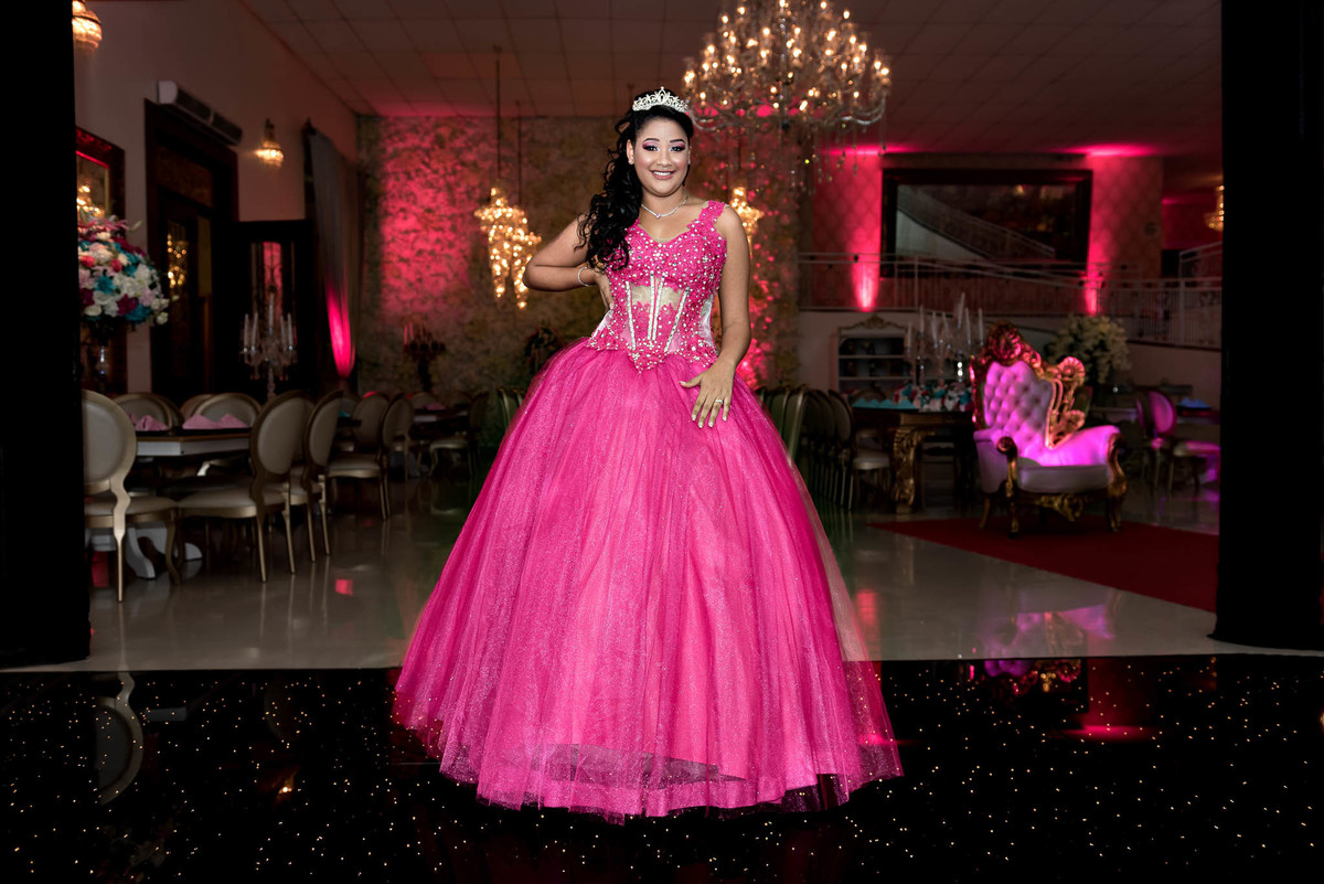 Jamile descendo uma escadaria de forma dramática em seu vestido rosa choque, com o vestido se espalhando, capturando um momento clássico de debutante