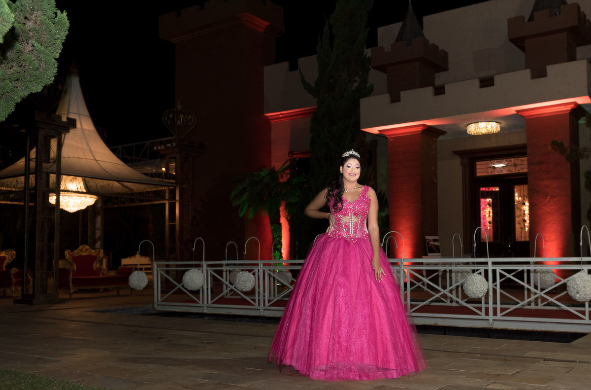 Jamile, a debutante, em seu vestido rosa choque, posando para uma foto com o vestido estendido no chão, destacando o caimento da saia