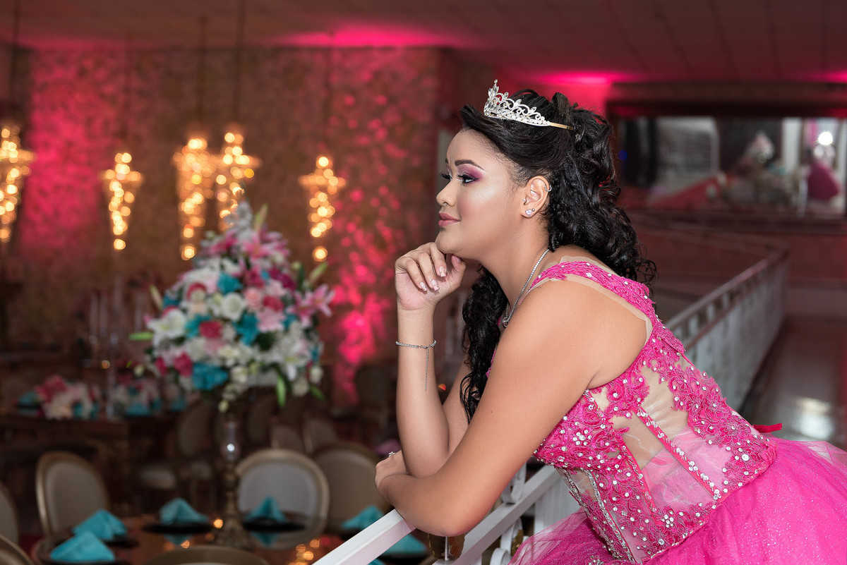 Jamile posando com o vestido rosa choque, em um ambiente com iluminação cênica e decoração em tons de rosa