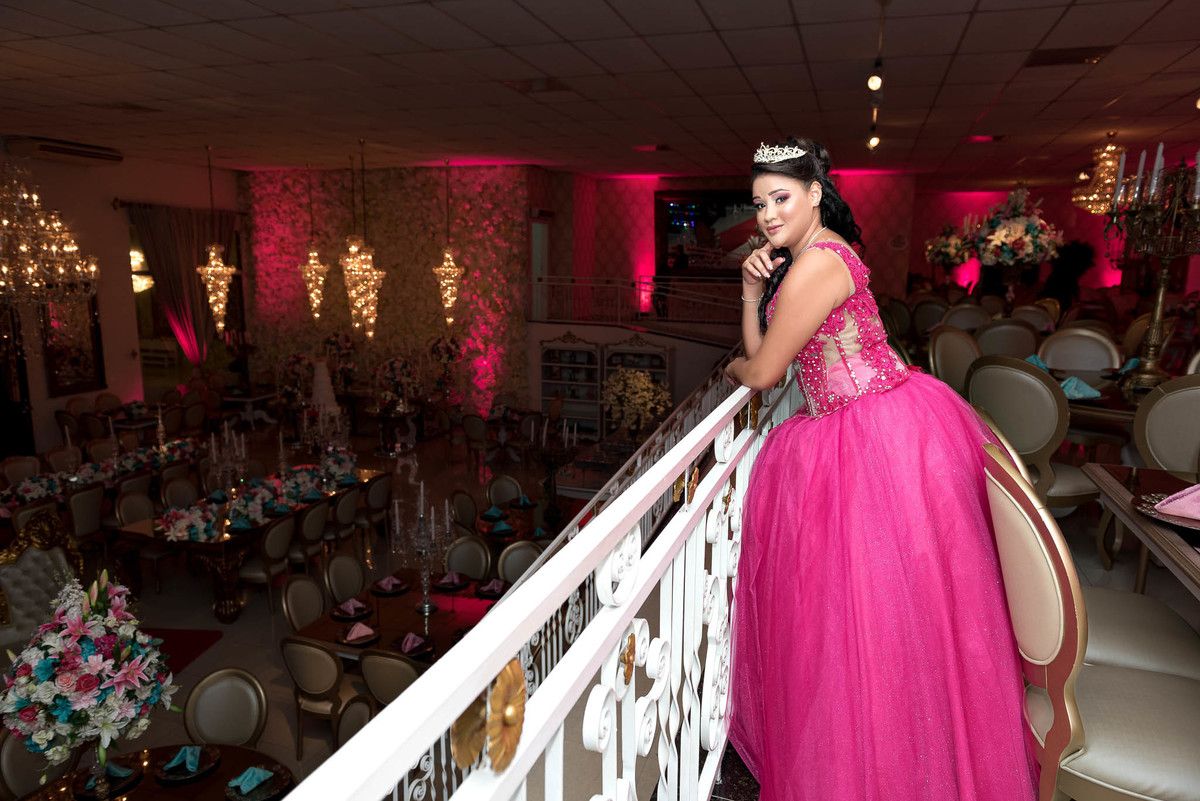 Jamile, de costas, descendo uma escadaria, com a longa cauda do vestido rosa choque em destaque, criando uma imagem dramática