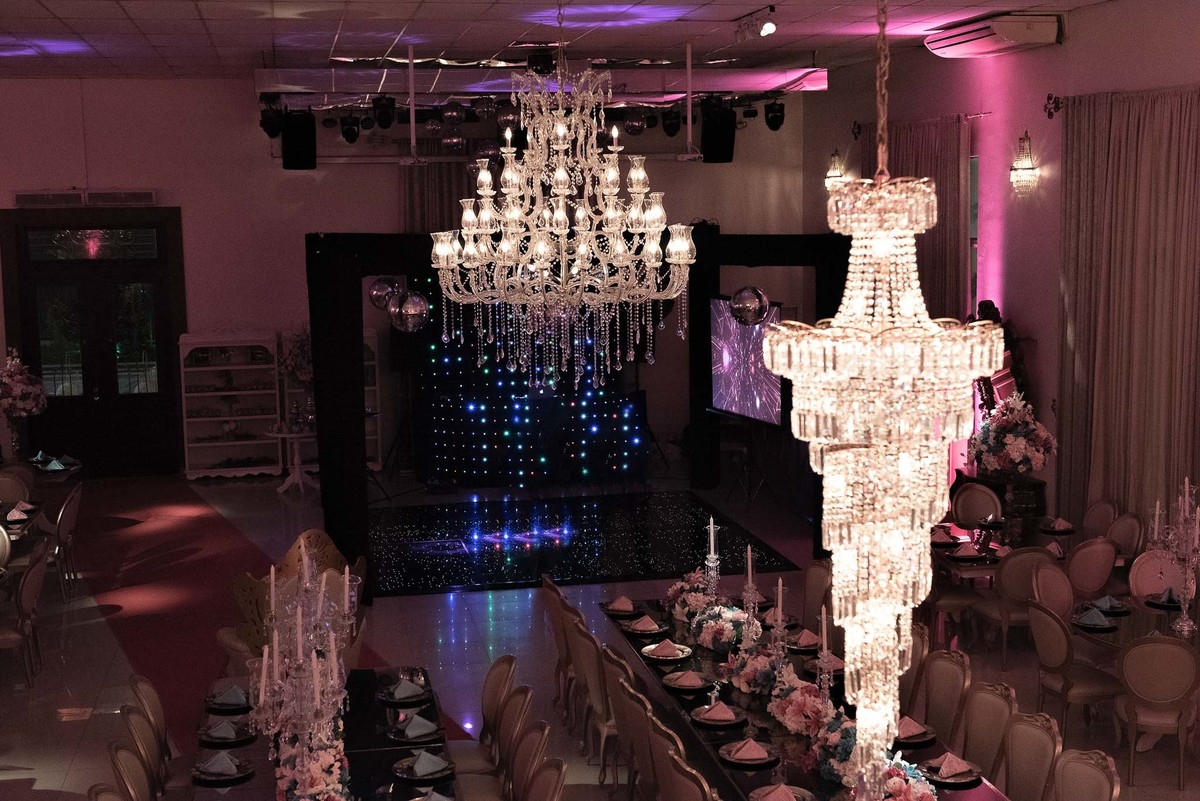 Jamile com um vestido claro, possivelmente branco ou marfim, dançando em um ambiente com iluminação de balada em tons de roxo e azul, mostrando a pista de dança