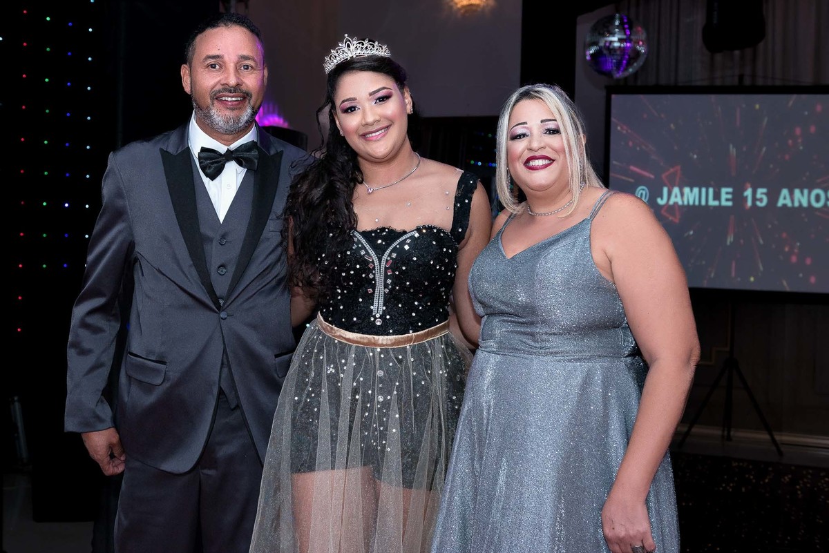 Jamile com seus pais ou familiares próximos, todos elegantemente vestidos em tons de cinza e preto, tirando uma foto em grupo