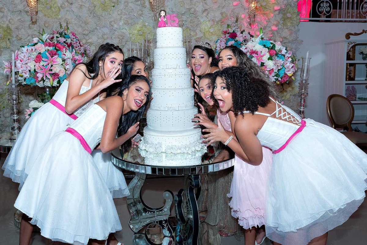 Jamile e uma amiga (ou familiar) se divertindo enquanto cortam o bolo de 15 anos, um momento clássico da celebração