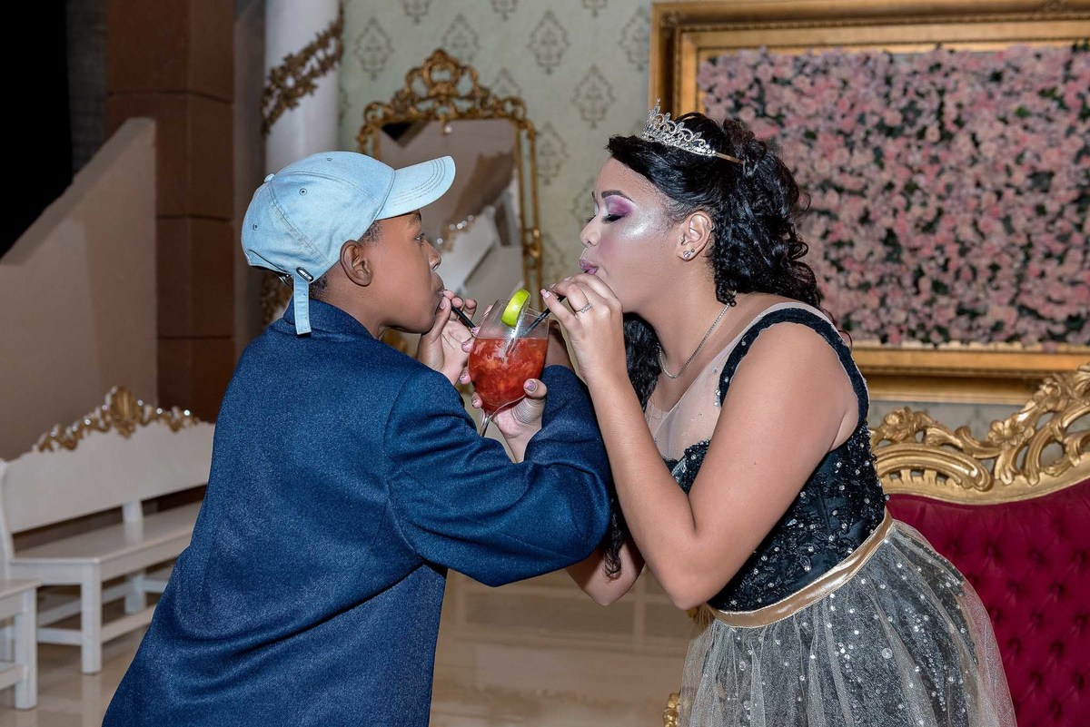 Jamile, em seu vestido pretobrincando com seu drink com o amigo, em um momento de carinho durante a festa