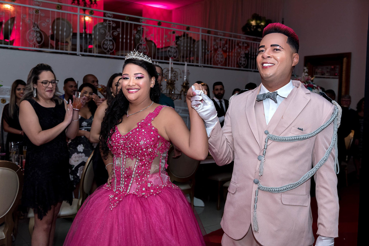 Jamile com o príncipe, ambos com adereços de festa, brindando com copos em um ambiente descontraído da festa