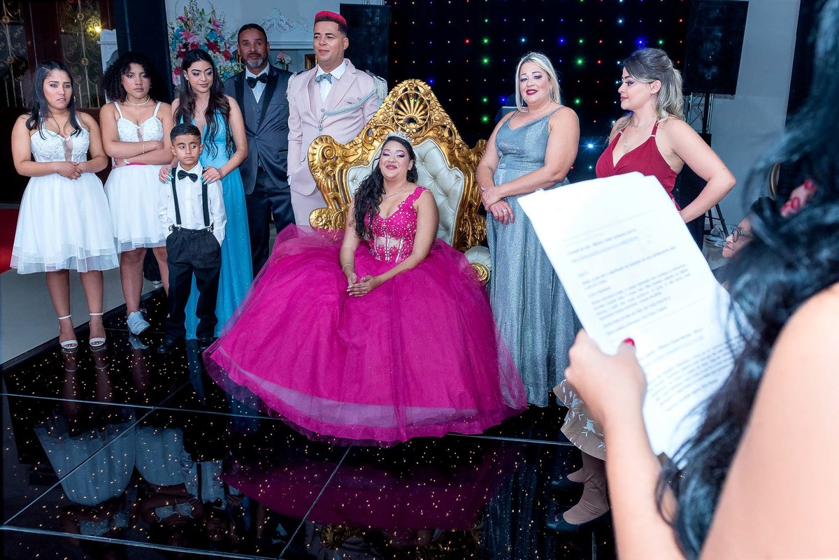 Jamile, em um vestido rosa curto, e um grupo de amigas em vestidos brancos, dançando juntas e se divertindo na festa de 15 anos