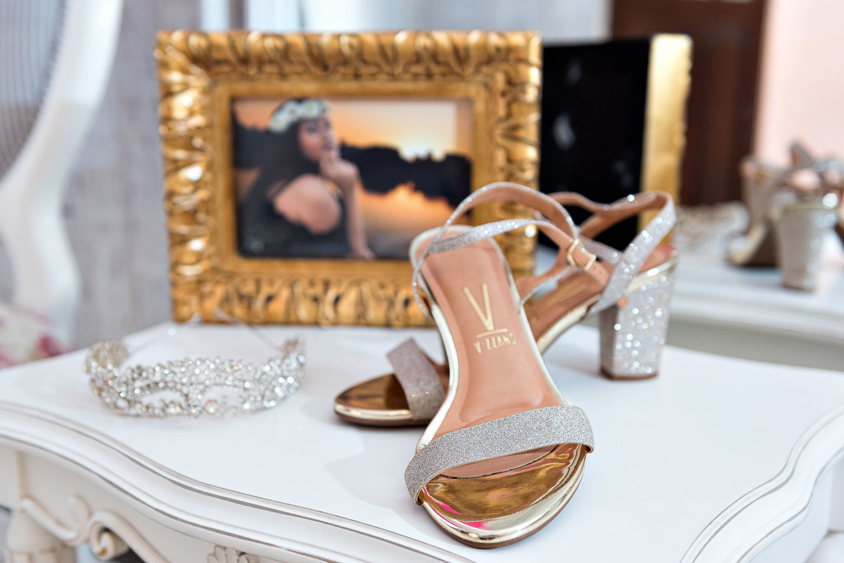 Detalhes dos acessórios da festa: um par de sapatos de salto alto dourados, um sutiã preto e um cinto dourado, sobre uma superfície clara e decorada