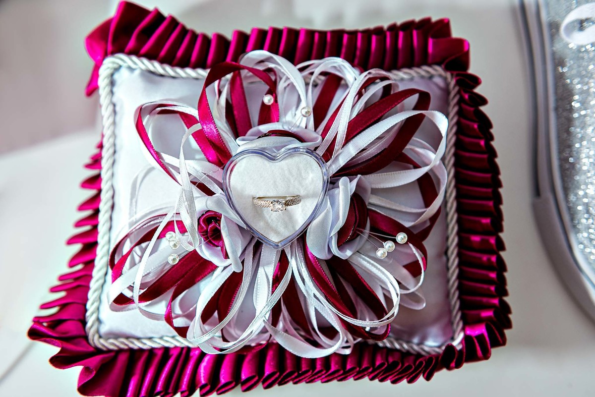 Detalhe de uma almofada decorativa de festa, com um laço e flores em tons de rosa e branco