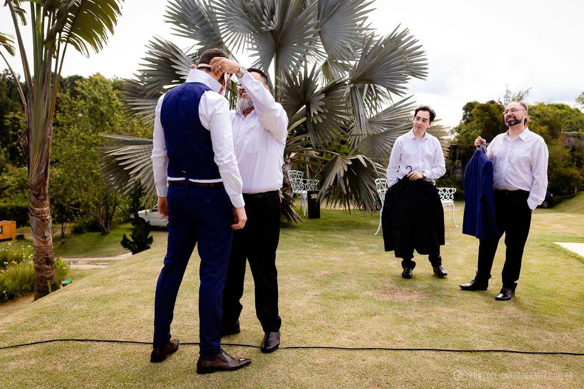 padrinho colocando a gravada no noivo padrinho olhando e segurando o terno do noivo
