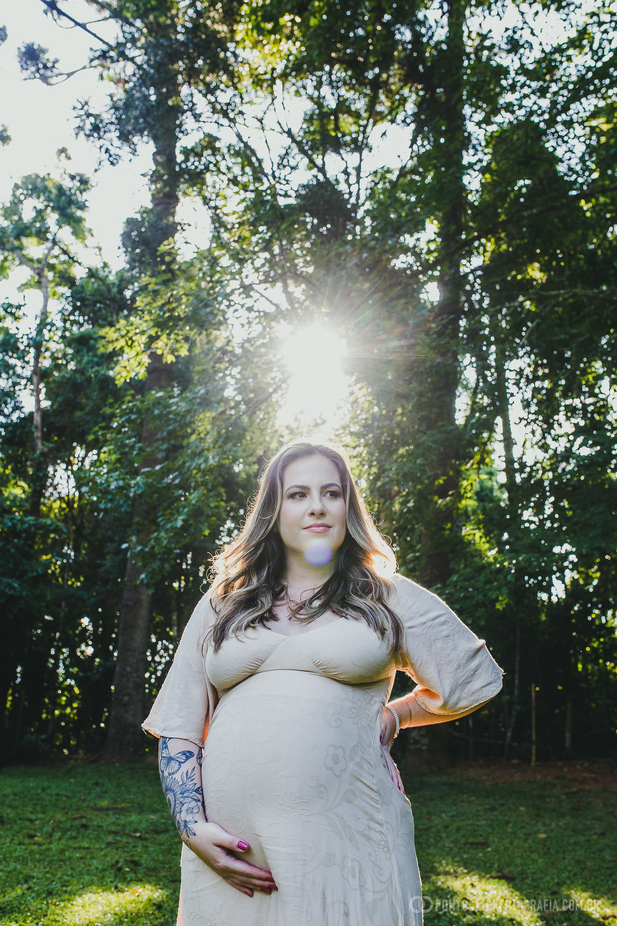 Retrato de uma futura mãe em um ensaio de gestante, com luz do sol iluminando os cabelos enquanto ela exibe serenidade e beleza. A cena natural reforça a conexão com a maternidade