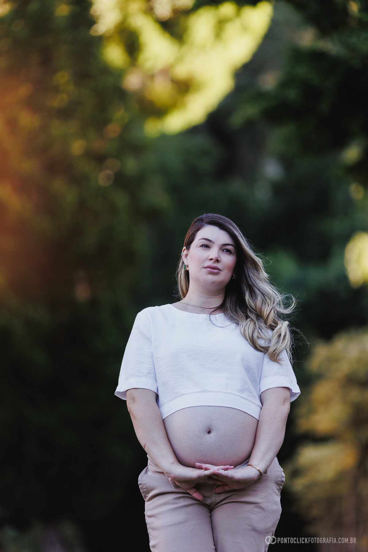 ensaio gestante natural com retrato central valorizando expressão, luz suave e conexão com a maternidade em ambiente externo com fundo verde desfocado