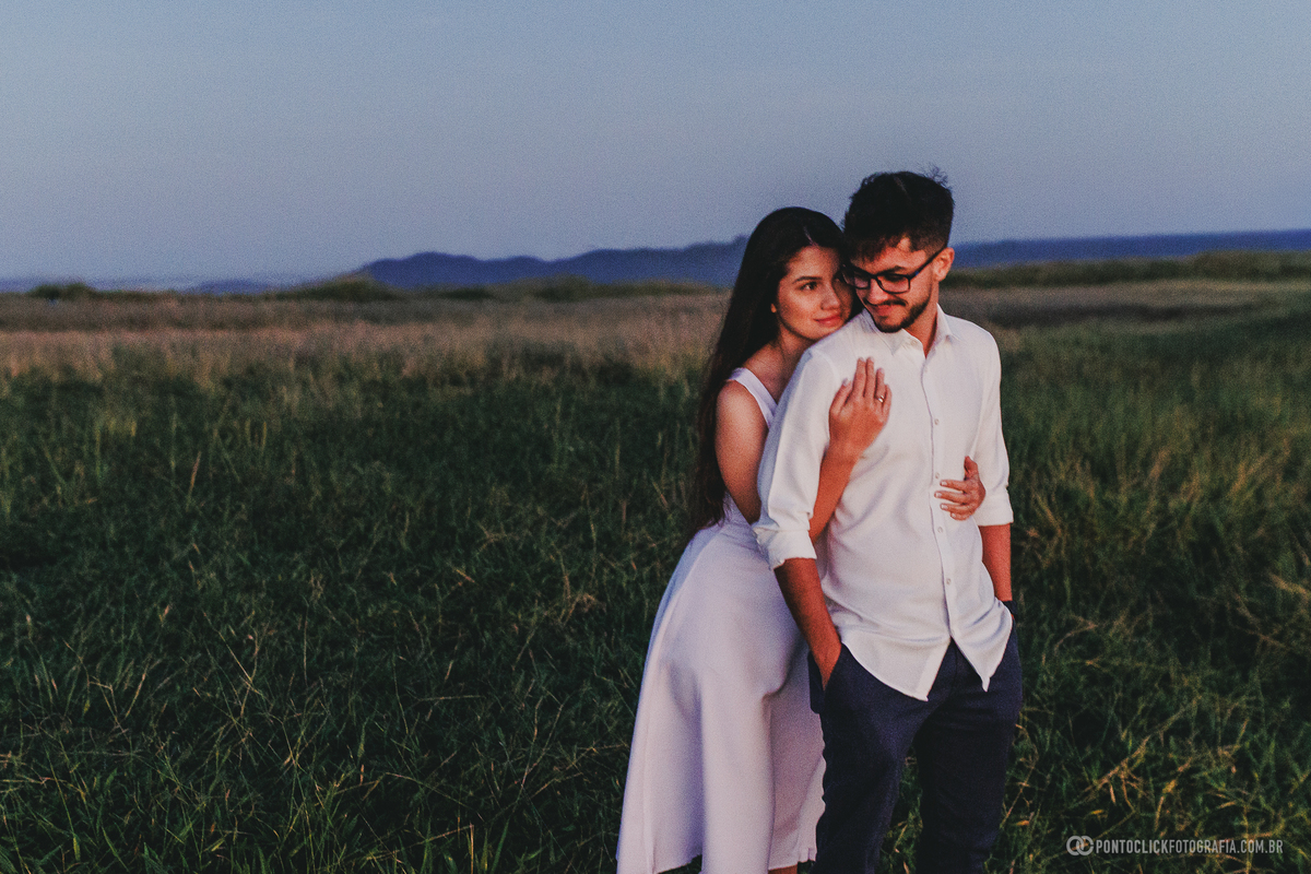 Casal em ensaio pré wedding no Morro do Capuava em Pirapora do Bom Jesus ao nascer do sol, caminhando em meio à vegetação com luz suave do amanhecer e paisagem natural ao fundo, criando um cenário romântico e leve ao ar livre
