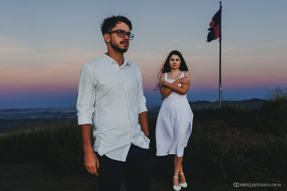 Casal em ensaio pré wedding no Morro do Capuava em Pirapora do Bom Jesus com sol nascendo ao fundo criando efeito de flare e iluminação intensa destacando silhueta e conexão