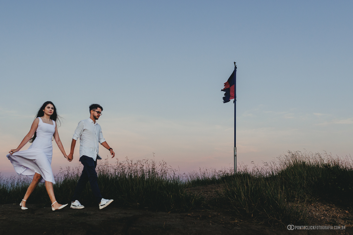 Casal em ensaio pré wedding no Morro do Capuava em Pirapora do Bom Jesus em meio à vegetação iluminada pelo sol criando cenário natural com tons quentes e atmosfera leve