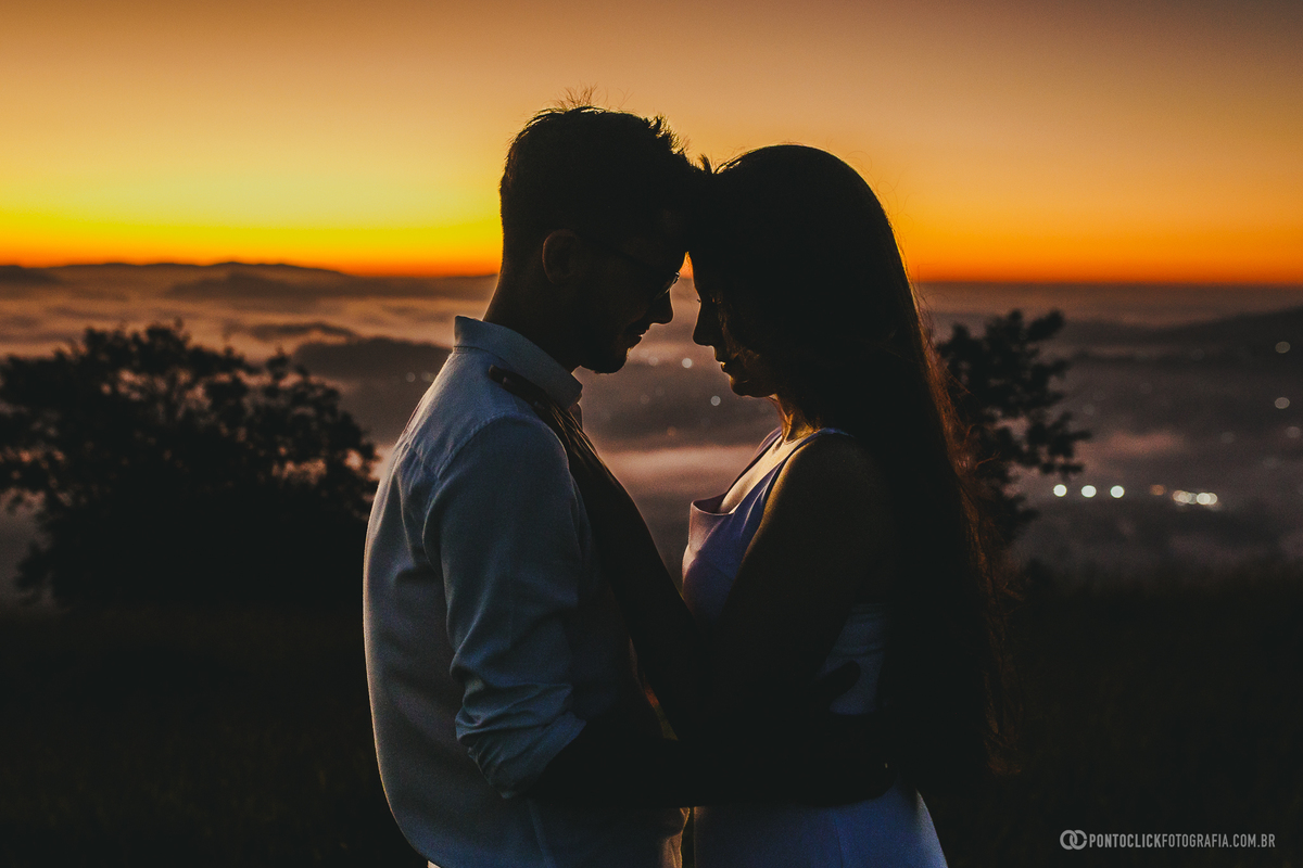 Silhueta de casal em ensaio pré wedding no Morro do Capuava em Pirapora do Bom Jesus durante o nascer do sol com mar de nuvens ao fundo, criando um cenário romântico com tons quentes e contraste forte no horizonte