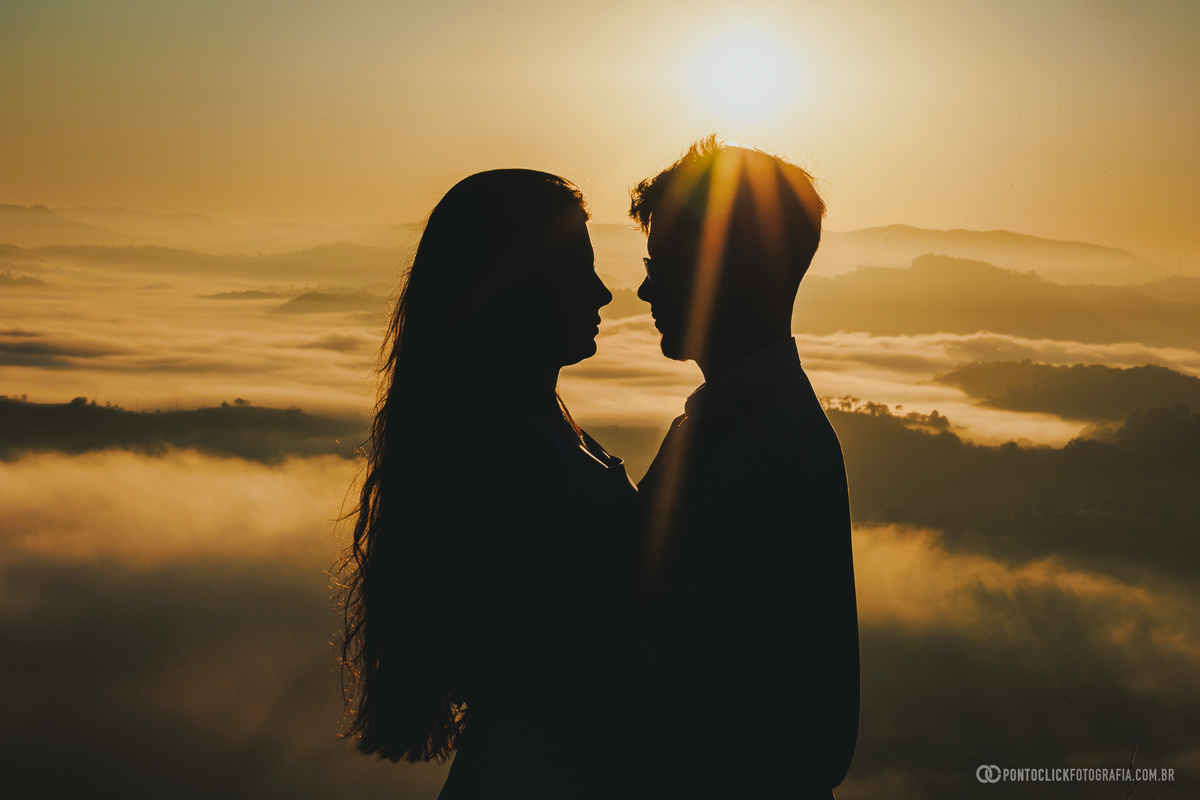 Casal em ensaio pré wedding no Morro do Capuava em Pirapora do Bom Jesus com luz dourada intensa ao amanhecer e mar de nuvens ao fundo criando silhueta romântica e composição impactante