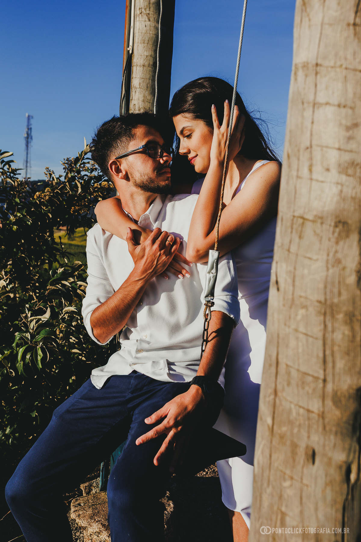 Casal em ensaio pré wedding no Morro do Capuava em Pirapora do Bom Jesus sentado em balanço de madeira com proximidade e conexão destacadas pela luz natural do nascer do sol