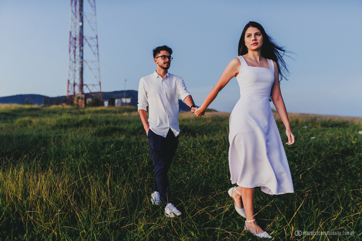 Casal caminhando de mãos dadas no Morro do Capuava em Pirapora do Bom Jesus durante ensaio pré wedding ao nascer do sol, com vegetação ao redor e céu aberto iluminado pela luz natural suave da manhã