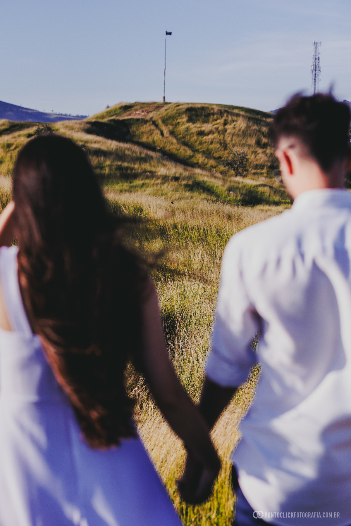 Casal caminhando de mãos dadas no Morro do Capuava em Pirapora do Bom Jesus durante ensaio pré wedding com vegetação ao redor e montanhas ao fundo criando movimento e leveza