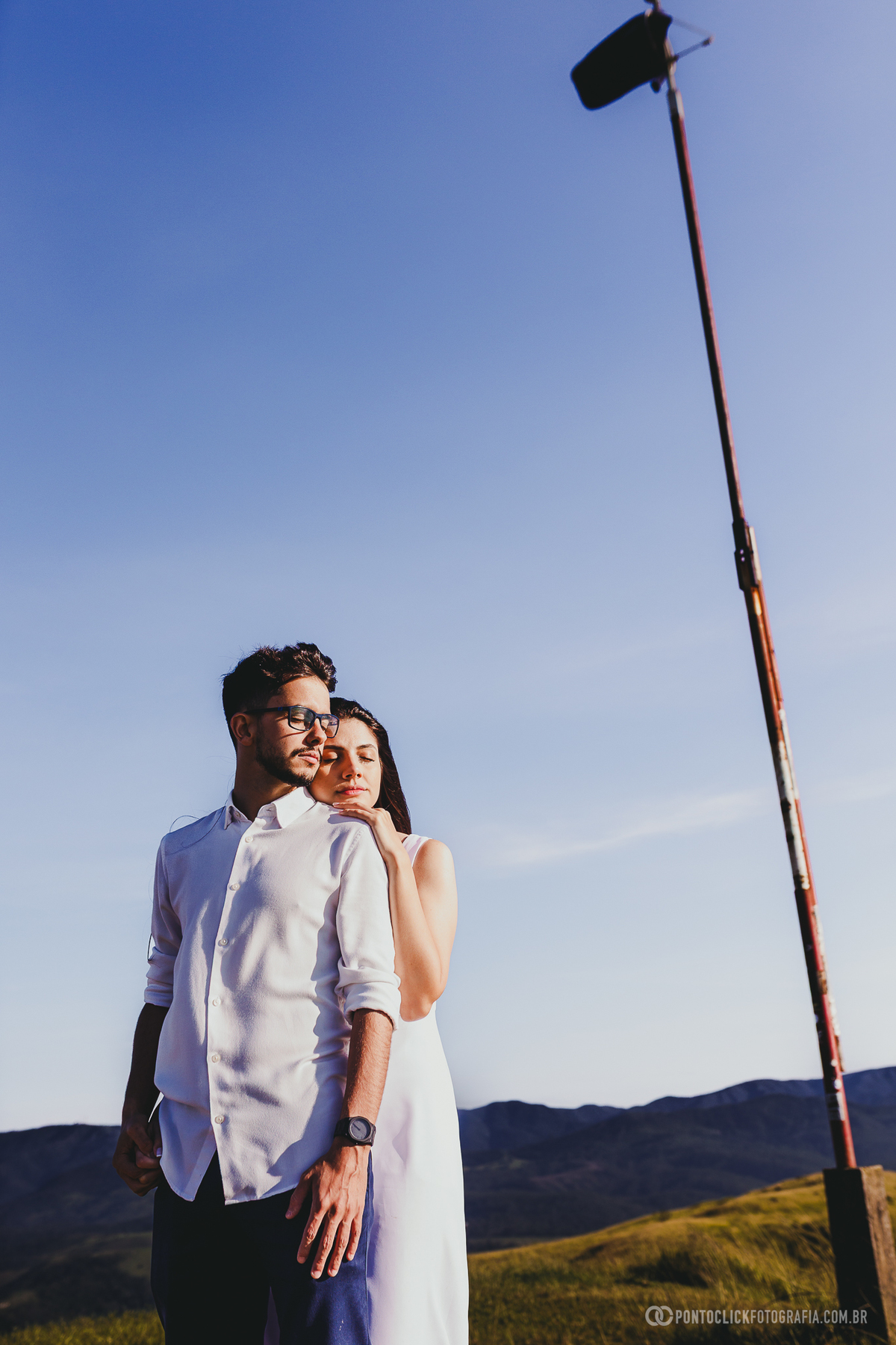 Casal em ensaio pré wedding no Morro do Capuava em Pirapora do Bom Jesus em plano aberto com luz intensa do nascer do sol criando silhueta suave e cenário amplo