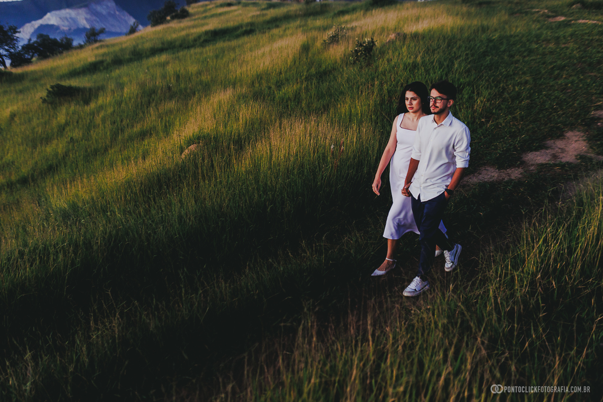Casal caminhando em trilha no Morro do Capuava em Pirapora do Bom Jesus durante ensaio pré wedding ao nascer do sol com vegetação ao redor e composição ampla valorizando o cenário natural